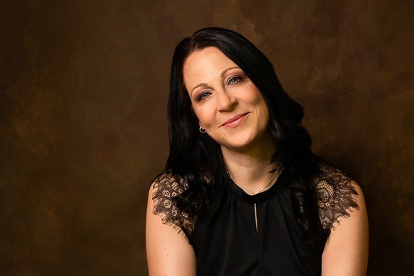 Eine Frau mit einem schwarzen Spitzenoberteil lächelt in die Kamera.