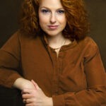 Eine Frau mit roten Locken sieht in die Kamera.